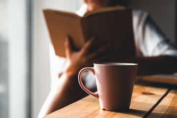 Woman in the morning drinks coffee and reads old book in a white shirt. Education, drink. manicure