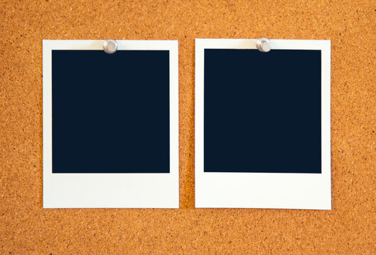Blank square Instant pictures pinned to a corkboard  with metal pushpins.