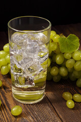 Fresh grape beverage with ice cubes in glass and bunch of sweet green grape on wooden table.