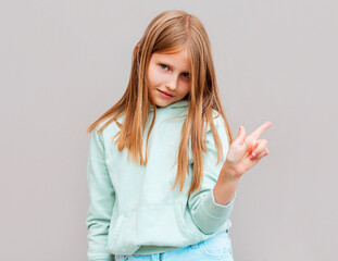 Cute cheerful blonde young female smiling broadly at camera and pointing fingers away, showing...
