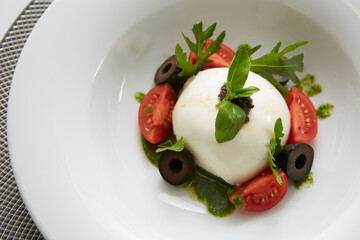 Traditional authentic soft and creamy fresh Italian burrata cheese shaped as white round ball over Italian tomatoes topped with rucola along side pesto reduction