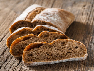 Ciabatta. Dark fresh healthy flattish open-textured Italian bread with a floury crust on wooden background. Close-up