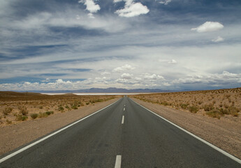 Traveling along the empty desert road. Asphalt highway across the arid valley and mountains under a beautiful sky. 