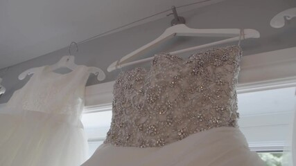 Canada - July 13, 2018: Beautiful white gown with bead sequence pattern hanging on hanger with gowns for bridesmaid in room near window