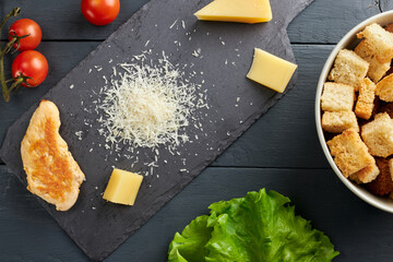 Top view of ingredients for making salad. Piece and grated parmesan cheese on black serving board,...