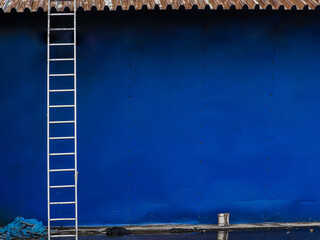 Blue background metal wall siding, cladding with stairs to the roof. Reflective metallic convex texture. Abstract ribbed backgrounds.