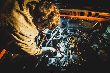 A man fixing an engine of a car at night. Vintage car being repaired during a night time. Bad...