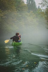 Back view of a green canoe in a misty and foggy river between the trees. Scary spooky and mistery exploration with a canoe on a river Krupa in Slovenia.