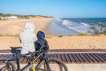 Back view of family looking at the beach, tourists use bicycles. Sunny blue sky outdoors background. Ecotourism activity concept.