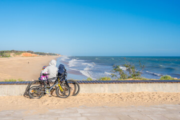 Back view of family looking at the beach, tourists use bicycles. Sunny blue sky outdoors background. Ecotourism activity concept.