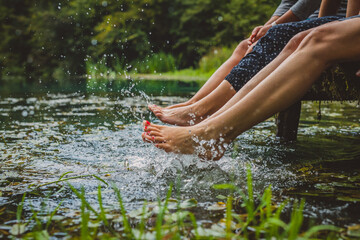 Detail of three young women with nice nails relaxing on a wooden pier and splashing their feet into...