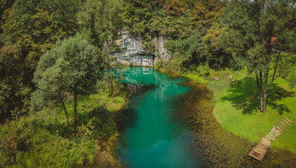 Aerial drone view of river source or spring of Krupa in Bela Krajina (White Carniola) in Slovenia on a misty cloudy day. Visible leaves and foggy green river with rock formation in the back.