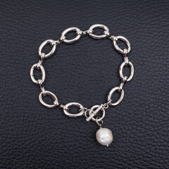 Fototapeta na wymiar Steel chain bracelet with baroque pearl pendant on black leather background