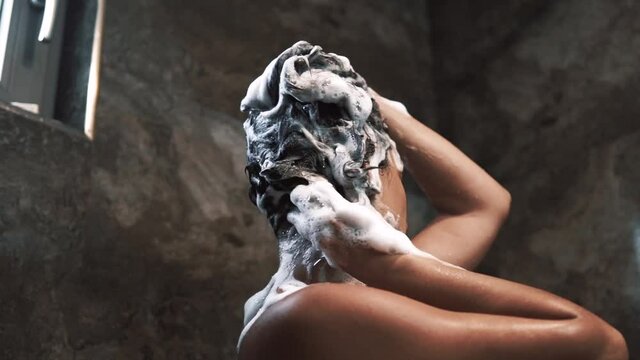 A woman washes short hair with shampoo in the shower cabin