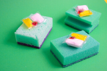 gel capsules for dishwashers and sponges on a green and yellow background of the places of the copy top view, the choice between washing dishes with your hands or in the dishwasher