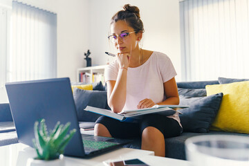 Front view on young caucasian woman study in front of the laptop computer at home - Girl reading book preparing exam test having online consultation - education and learning concept - obrazy, fototapety, plakaty