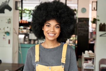 Happy stylish African American gen z hipster female student with Afro hair looks at camera stands...