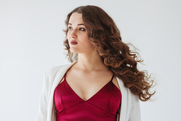 A beautiful curly pregnant girl in a dark pink evening dress and long white jacket is on a white background. (selective focus on one eye)