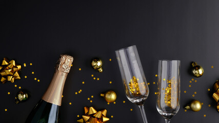 Christmas composition. Champagne bottle, glasses, golden confetti and balls decorations on black...