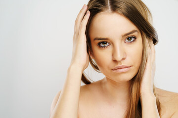 Naklejka premium Beauty portrait of beautiful caucasian girl young brunette woman with natural perfect skin and makeup holding hand in hair looking to the camera at studio in front of white background copy space