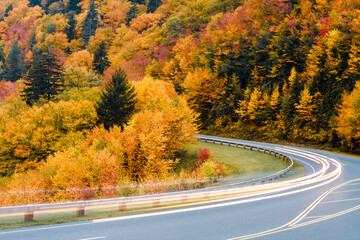 Blurred car lights on a mountain road against a colorful Autumn scene.