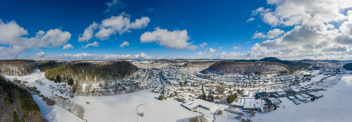 Idyllic town in a snowy winter, filmed from above, a drone shot in the Swabian Alb with hills and a part of a forest.