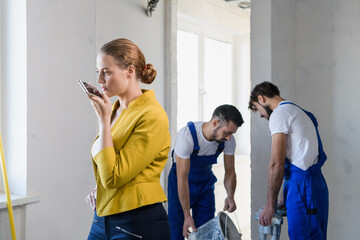 A inspector speaks on a cell phone. Two builders stand in the background