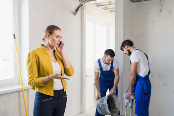 Two workmen are preparing cement in a bucket. Woman speaks seriously on the phone