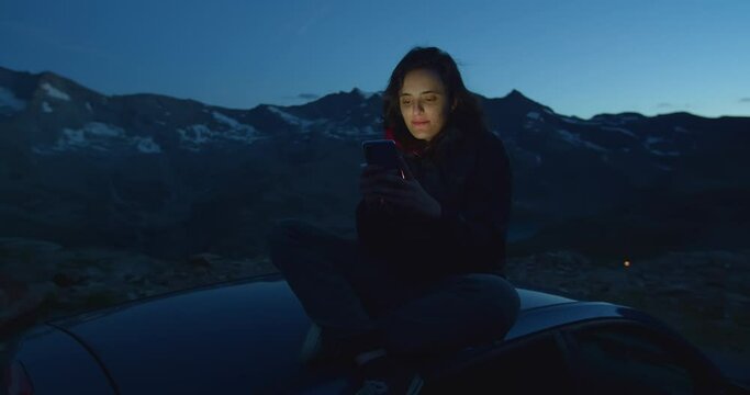 Woman communicates online, typing text on the phone, millennial sitting in a car in the mountains in nature, manager enjoys a vacation in Europe, travel and remote work concept