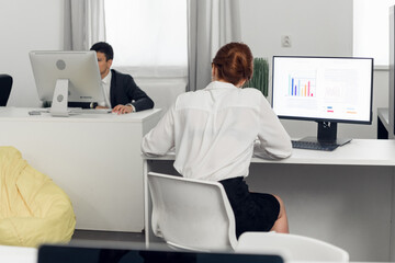 Girl Manager in a white blouse at the computer calculates the profit and loss of the company, builds charts