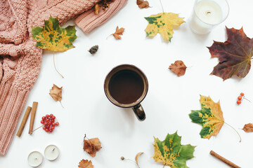 Knitted sweater, cup of coffee, autumn leaves, cinnamon sticks, candles on white background. Autumn composition. Flat lay, top view, copy space