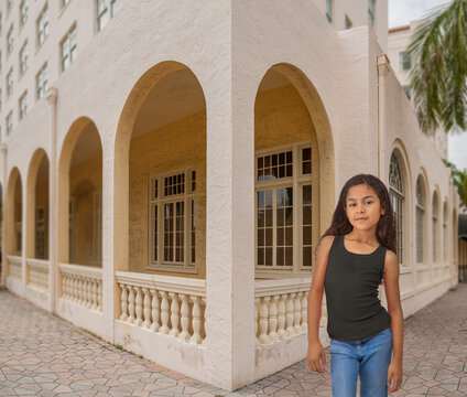 A young girl walks by an abandoned old hotel and asserts herself while checking out the area. She walks with confidence, wearing blue jeans and a black tank top.