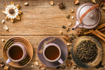 Tea in purple cup on purple saucer and brown saucer Brewed from dried tea leaves Designed with purple teapot and cinnamon with white flowers on wooden background.