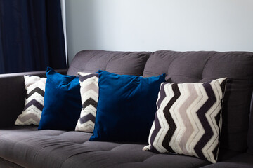 portrait of a livingroom, with white, black and blue cushions, with a white wall, navy blue curtains and a gray sofa