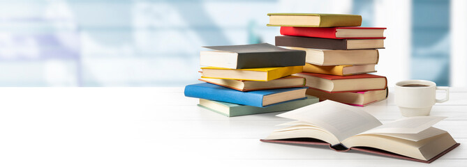山積みの本、コーヒー、開いた本のある白いテーブル。読書、勉強のイメージ