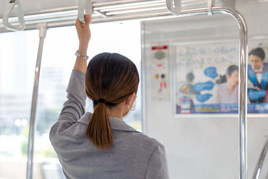 マスク姿でつり革に掴まって電車通勤をする女性