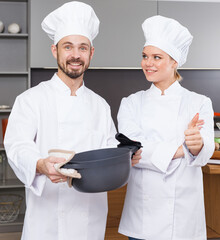 Happy professional chefs in white uniform standing together in home kitchen .