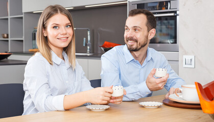 Happy young couple enjoying conversation over cup of coffee in stylish kitchen interior.