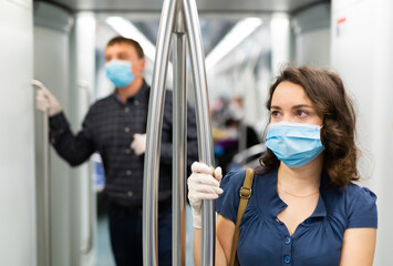 Portrait of focused woman in disposable mask and gloves traveling in subway train during daily commute to work in spring day. Concept of new life reality and precautions in COVID 19 pandemic