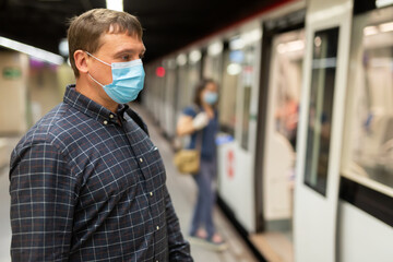 Fototapeta na wymiar Male in protective medical mask and gloves is traveling and waiting train on platform in the metro.