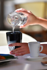 Close up of female hands pouring water from a jar into a cup on an out of focus background. Lifestyle concept.