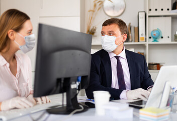 Portrait of confident manager wearing medical mask and protective gloves working with female colleague in office. New life reality during coronavirus pandemic