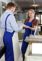 Fototapeta na wymiar Portrait of man and woman in blue overalls working in glass workshop..