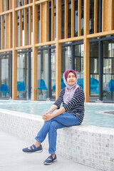 Asian muslim woman with brown eyes in scarf sitting at pool and smile