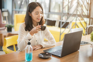 Smiling Asian businesswoman working on a laptop at her desk. Businesswoman in quarantine for coronavirus with alcohol gel.