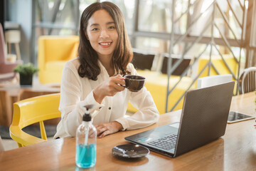Smiling Asian businesswoman working on a laptop at her desk. Businesswoman in quarantine for coronavirus with alcohol gel.