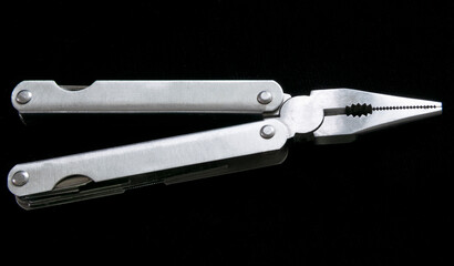 Multi-purpose steel tool on a black background, pocket knife and multi-tool for domestic use.