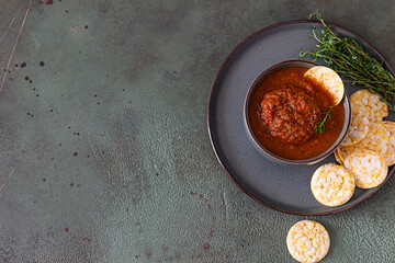 Ceramic bowl with spicy tomato sauce, tortilla chips and thyme on green background. Mexican food concept. Copy space. Top view.