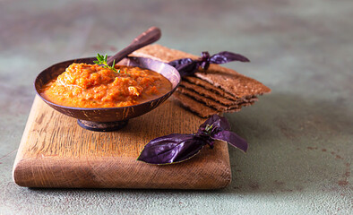 Multigrain crackers with homemade eggplant or zucchini caviar in a wooden bowl, green background....