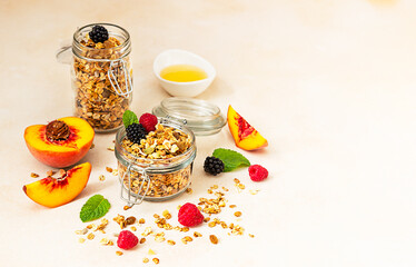 Homemade crunchy granola in glass jar, peaches, berries, honey and mint, light background. Healthy...